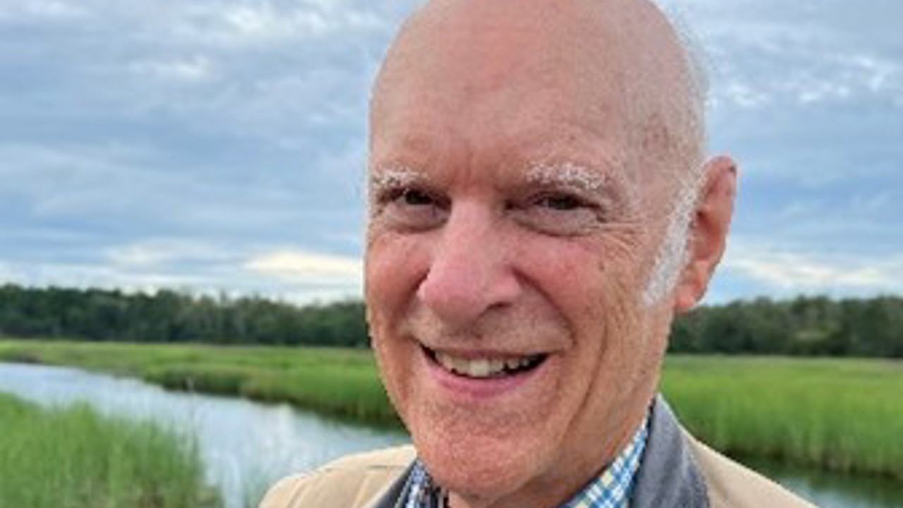 The picture shows Peter in a brown jacket and striped-blue shirt. There are grasslands in the background.