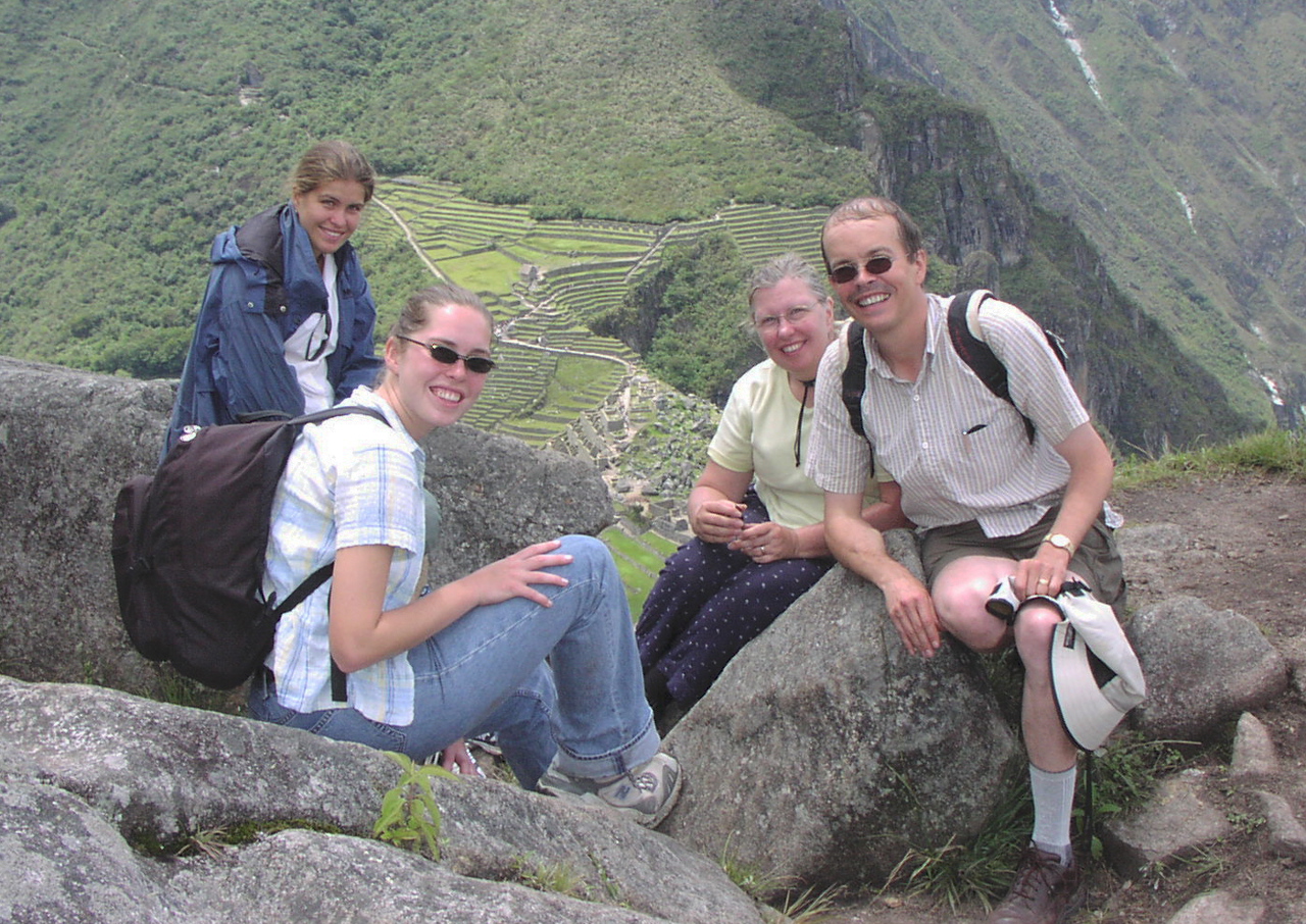 Rob and family sat on rocks on top of Machu Pitchu, smiling, wearing backpacks.