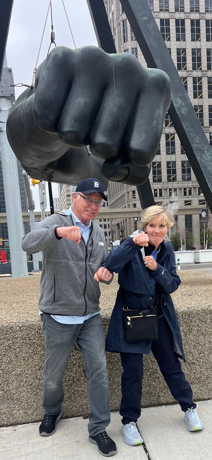 Behind Mary and Terry is a large statue of a fist. They are both stood posing in front of it with their fists out, mimicking the statue.