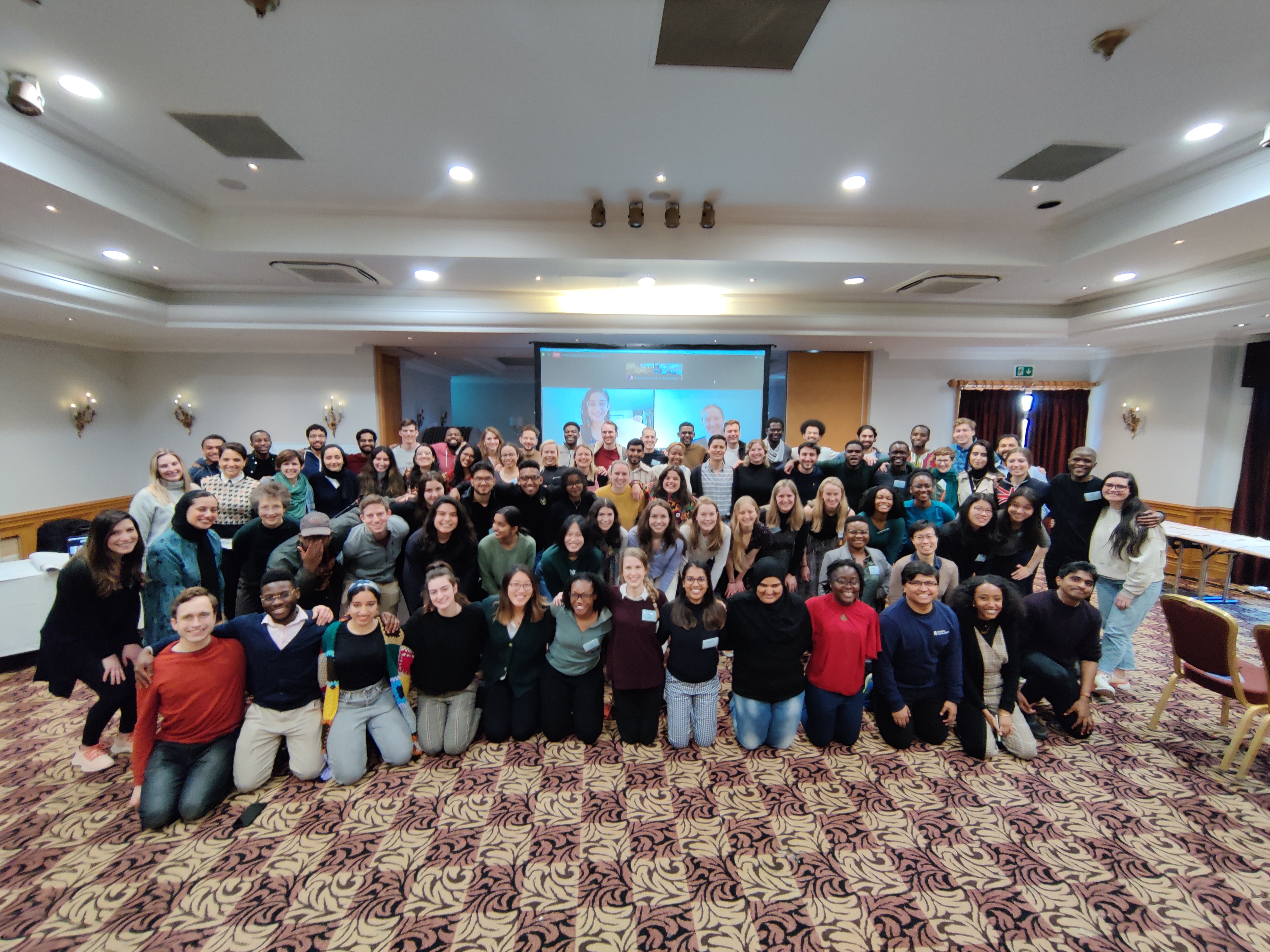 An indoor conference room filled with a group of around seventy students smiling and posing for the camera with their arms around each other as part of the Character, Service and Leadership Programme.
