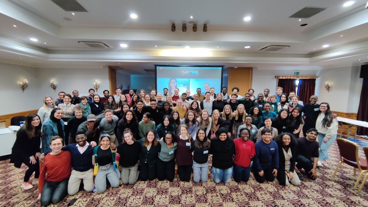 An indoor conference room filled with a group of around seventy students smiling and posing for the camera with their arms around each other as part of the Character, Service and Leadership Programme.