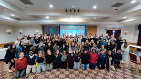 An indoor conference room filled with a group of around seventy students smiling and posing for the camera with their arms around each other as part of the Character, Service and Leadership Programme.