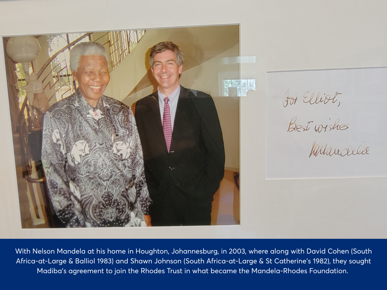 Photo of a framed image of Elliot standing to the right of Nelson Mandela, both smiling. The text to the right is a message from Nelson to Elliot saying 'best wishes'. Elliot was with Nelson Mandela at his home in Houghton, Johannesburg in 2003, where along with David Cohen (South Africa-at-Large & Balliol 1983) and Shawn Johnson (South Africa-at-Large & St Catherine's 1982), they sought Madiba's agreement to join the Rhodes Trust in what became the Mandela-Rhodes Foundation.