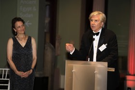 Elliot stood at a podium giving a talk, Elizabeth Kiss stood to the right and smiling.