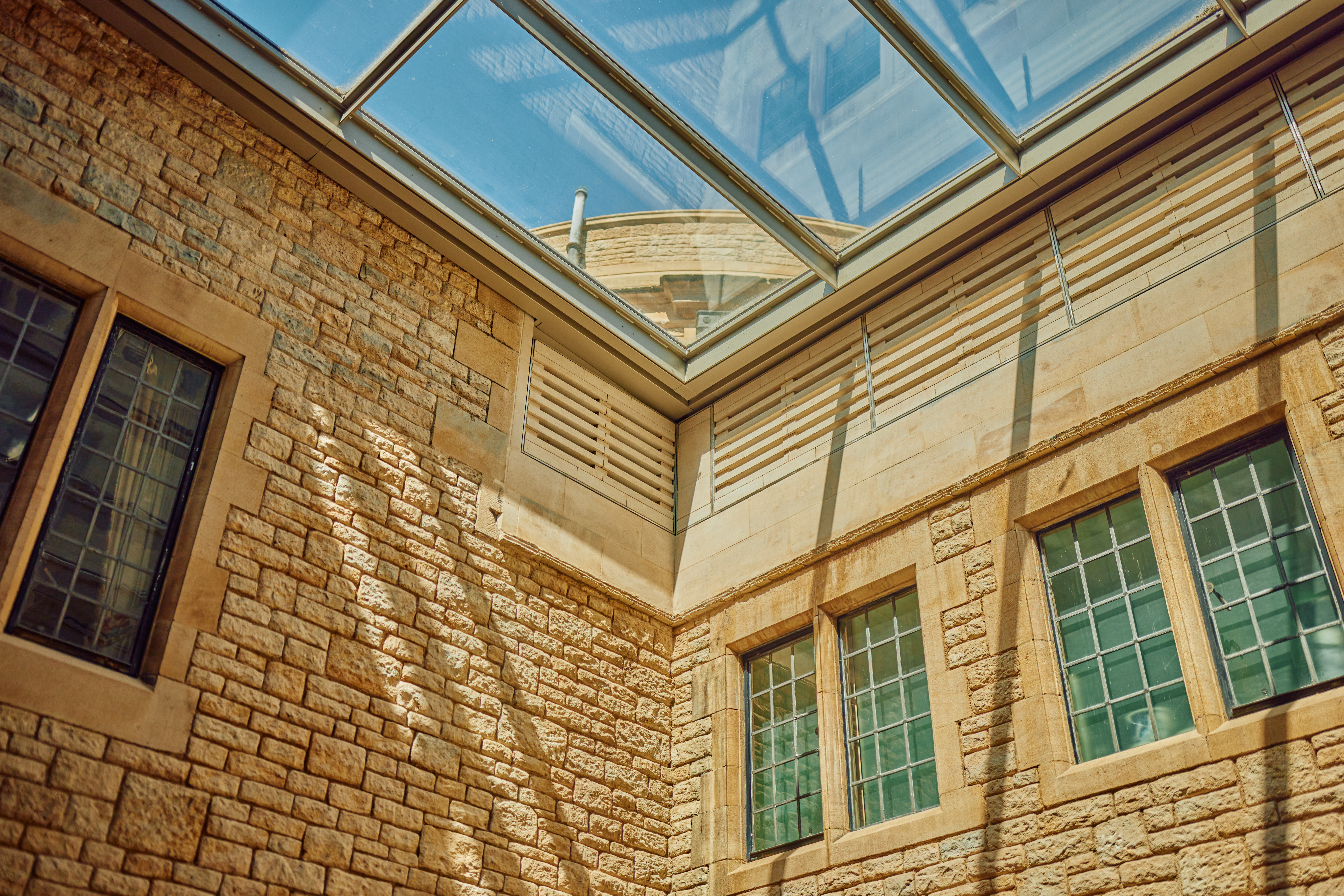 Image of a glass roof shown from the inside of a stone building. The sun is shining and gives the space a bright and airy look.