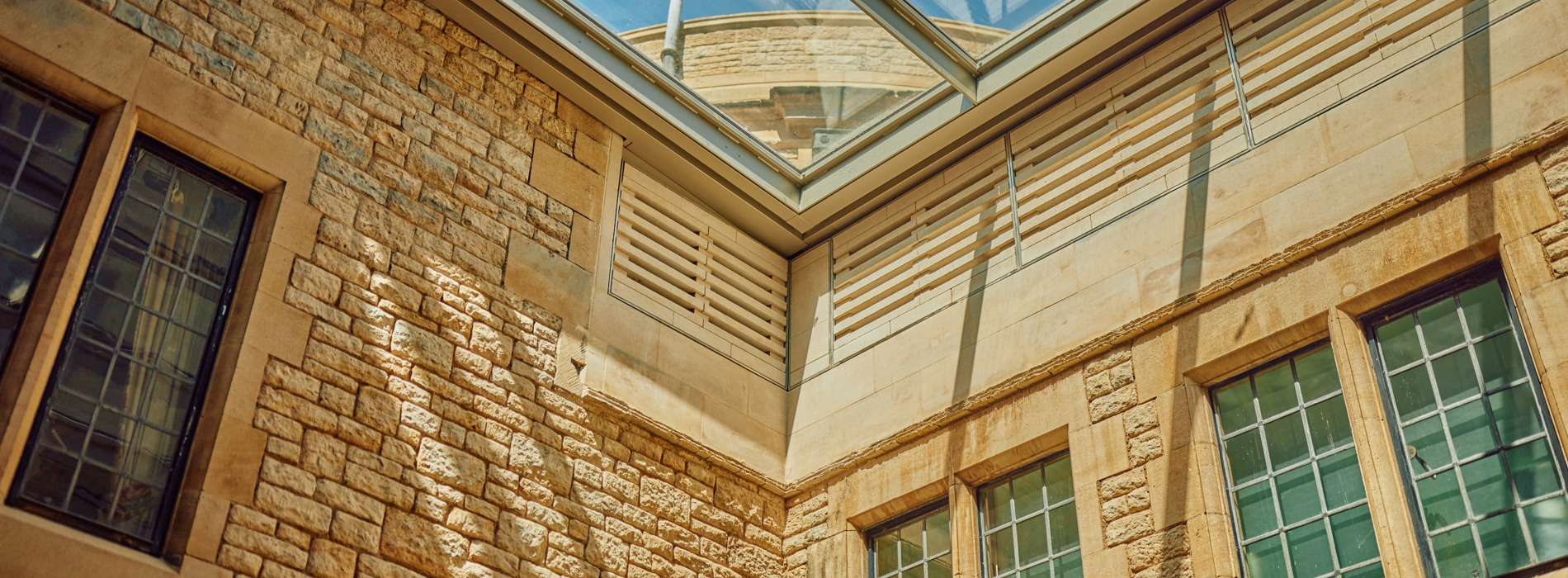 Image of a glass roof shown from the inside of a stone building. The sun is shining and gives the space a bright and airy look.