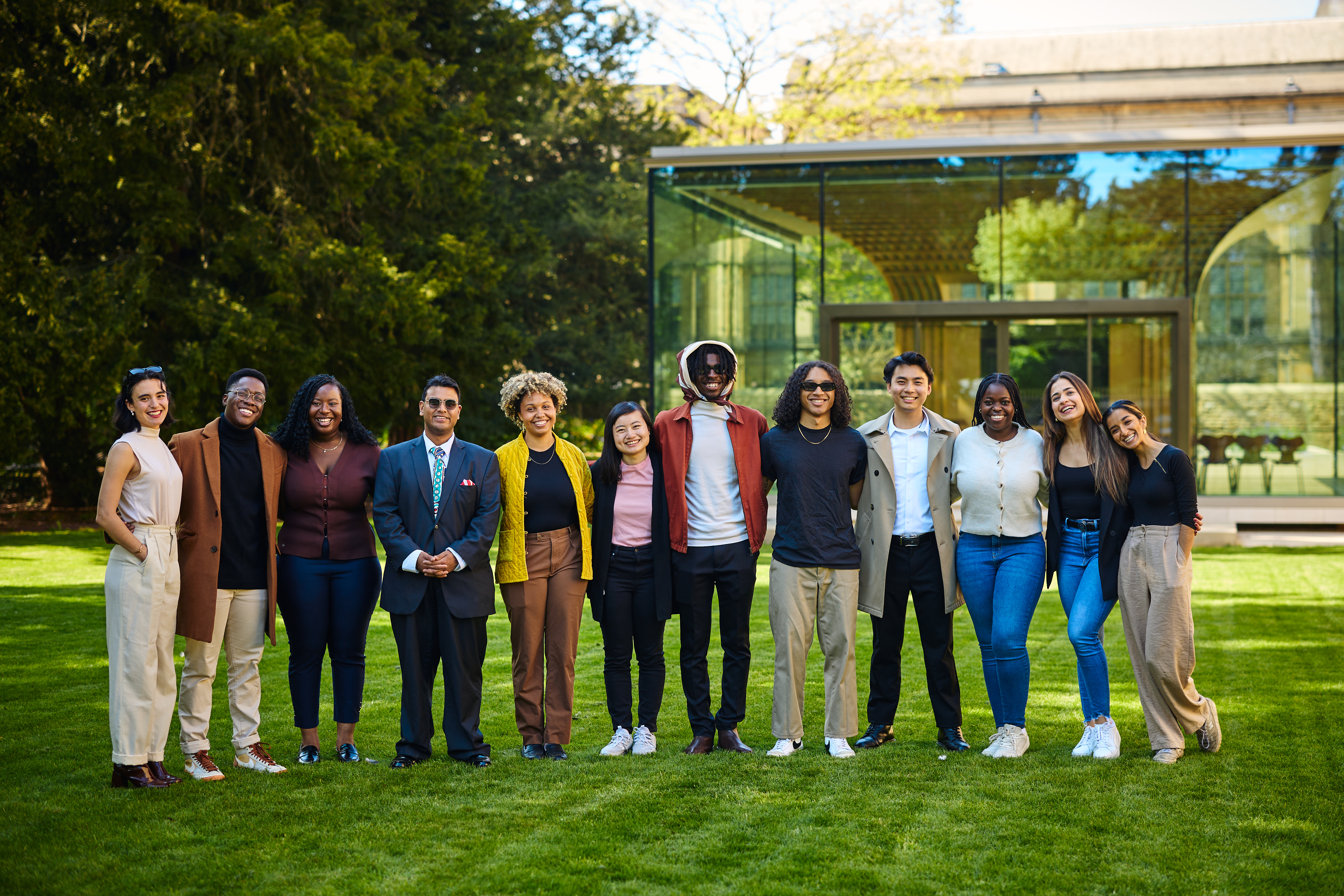 A diverse group of Rhodes Scholars posing together for a photograph on the lawn in Rhodes House, donning a vibrant variety of clothing.