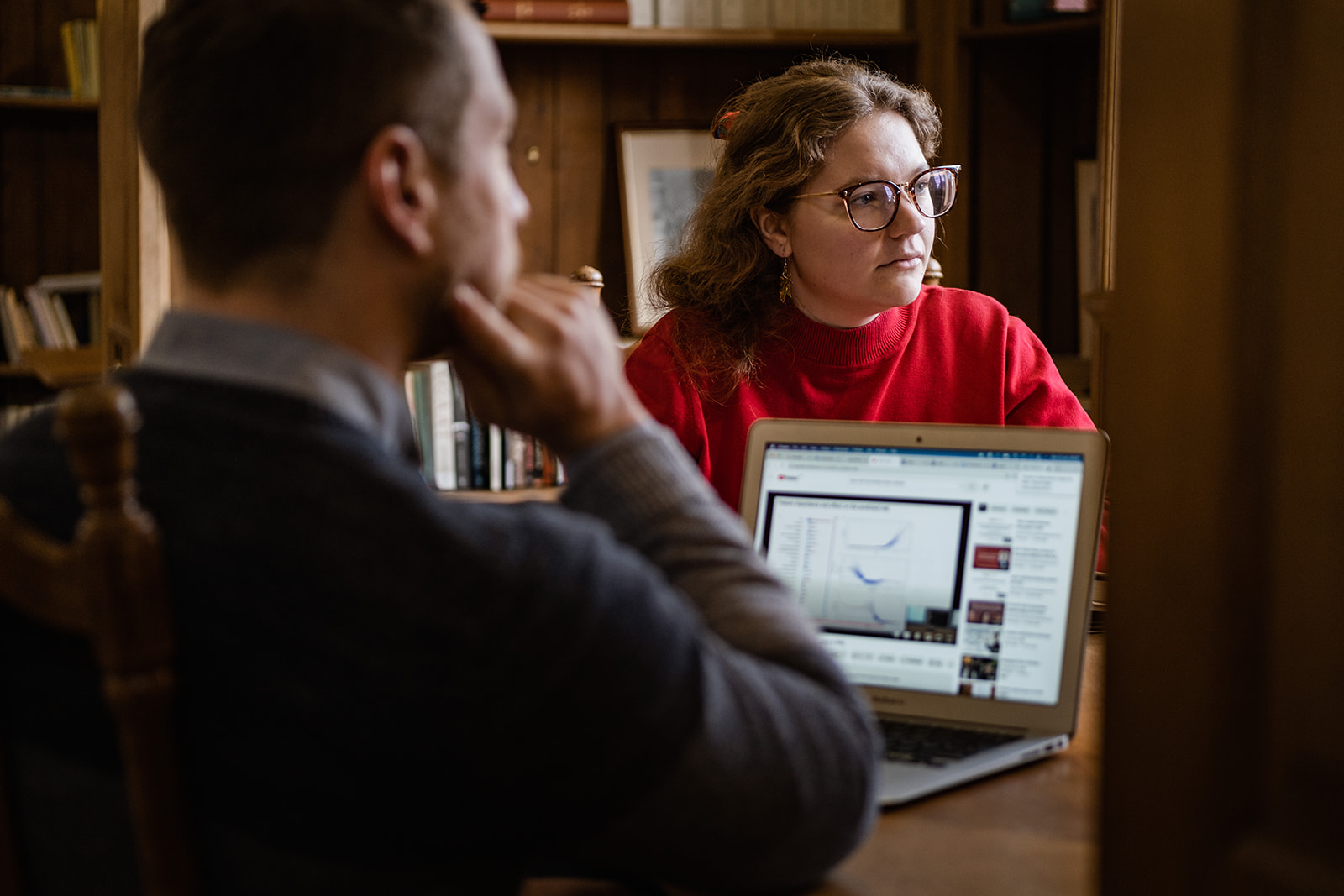 An image of two Rhodes scholars, a white man and woman, sitting opposite each other at a desk with an open laptop between them.