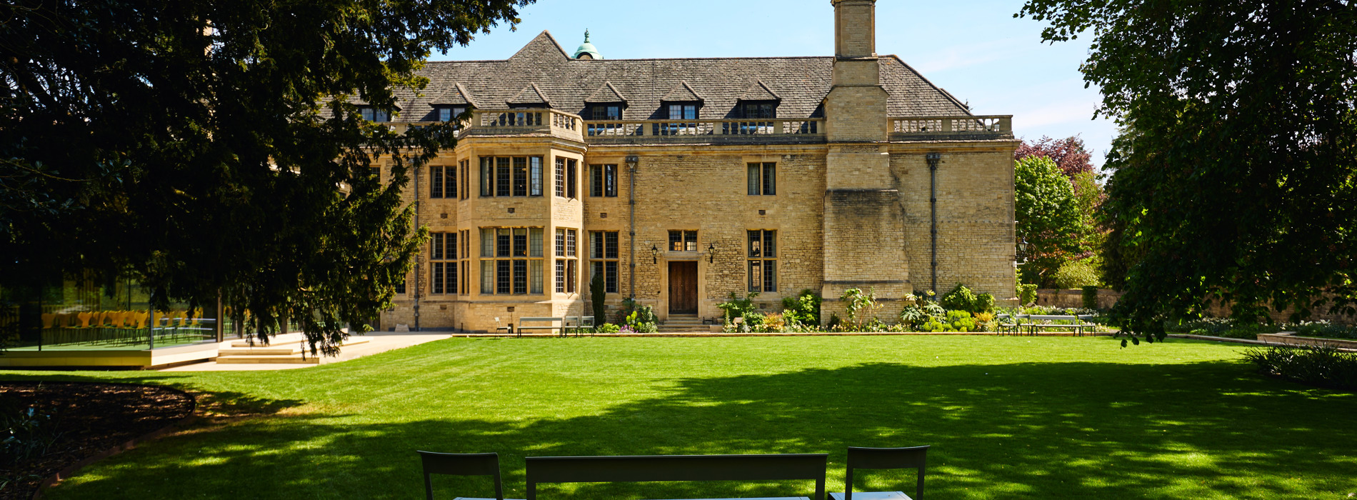 Daytime view of the west gardens with Rhodes House in the background and garden furniture in the foreground in the shade.