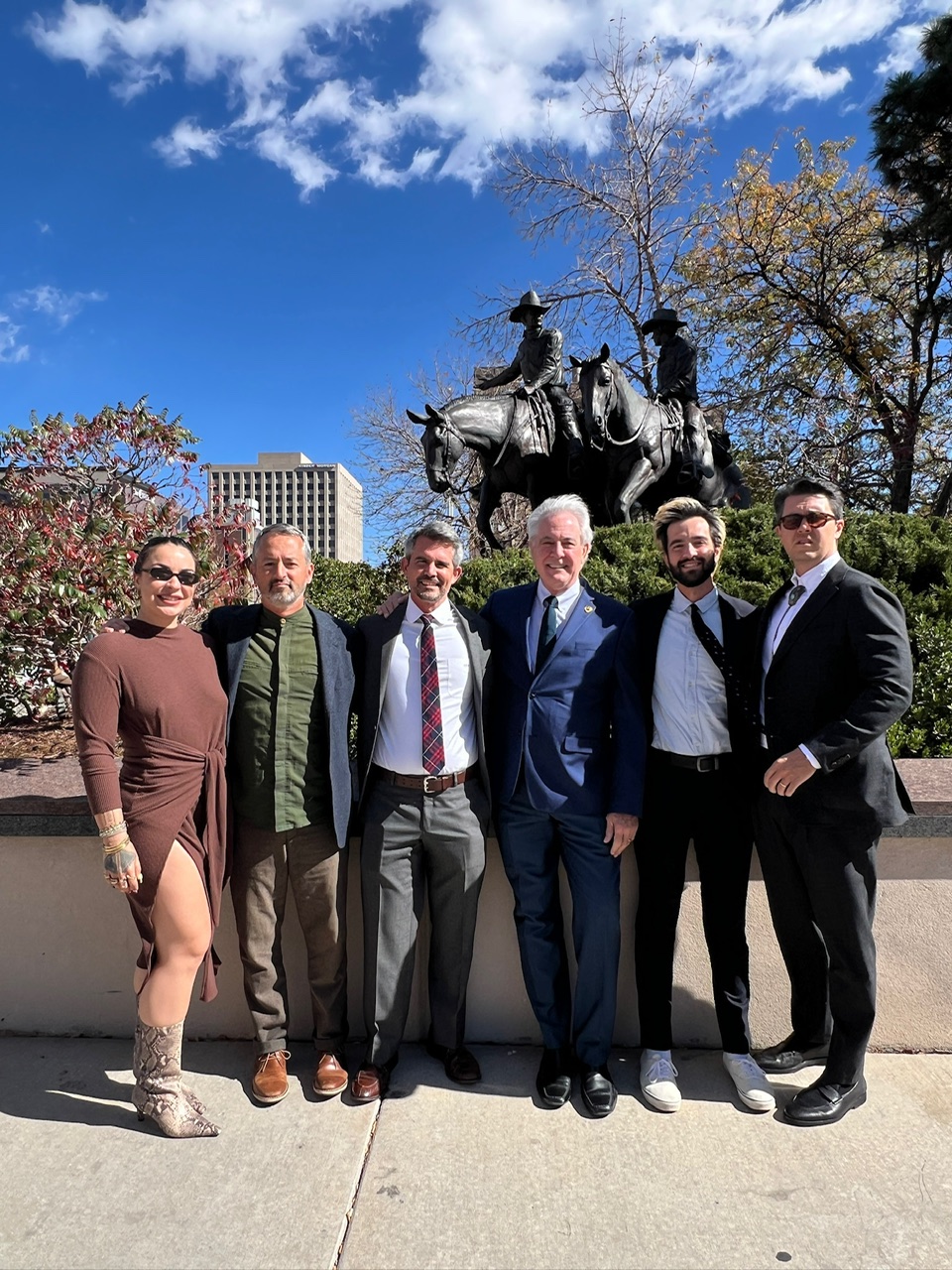 Ken is stood in the middle of his adult children. Behidn them, a black statue depicts two cowboys riding on horse