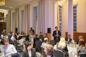 The picture shows Philip standing in a room full of people. They are all turned towards him.
