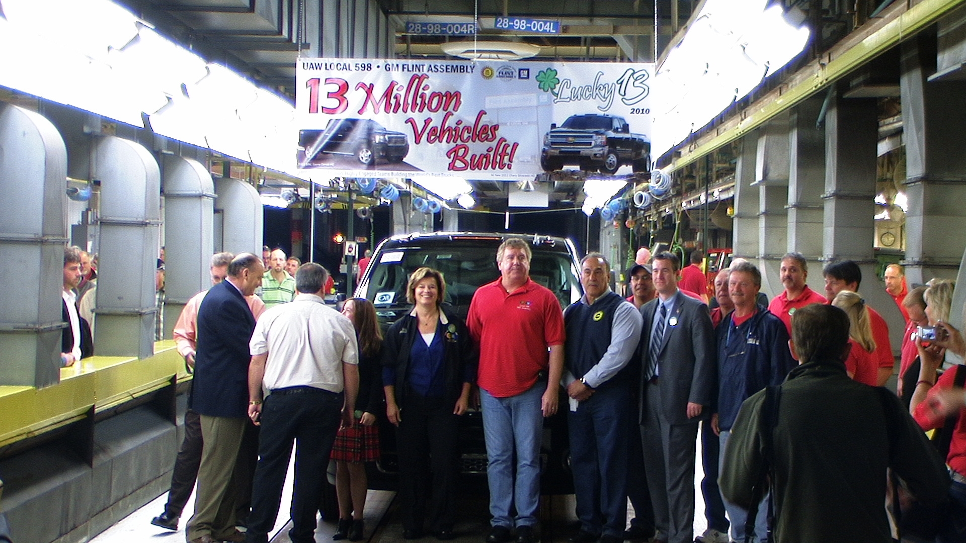 A large crowd is gathered before a car with a banner above them reading '13 Million Vehicles Built!'