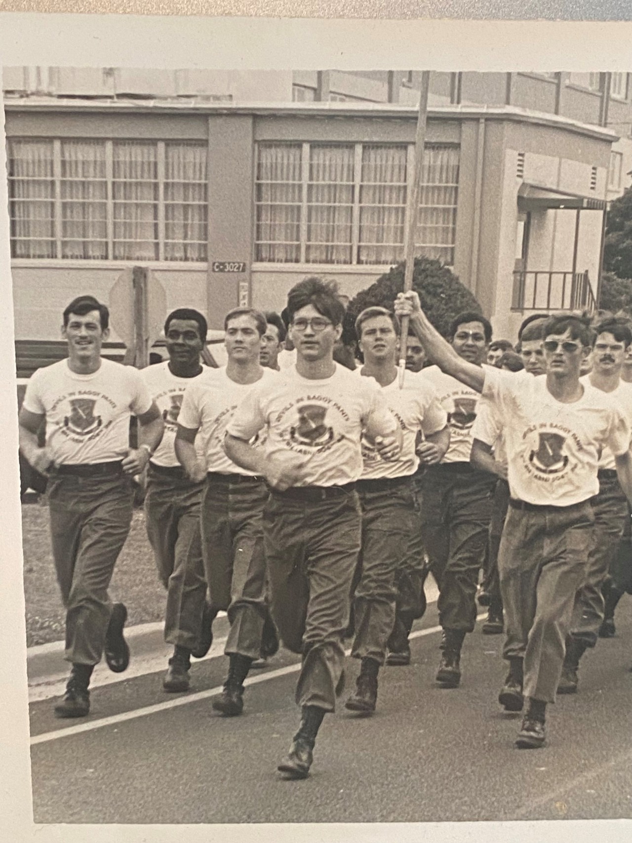 A black-and-white picture showing Jack leading a run of a group of soldiers in t-shirts, military pants and boots.