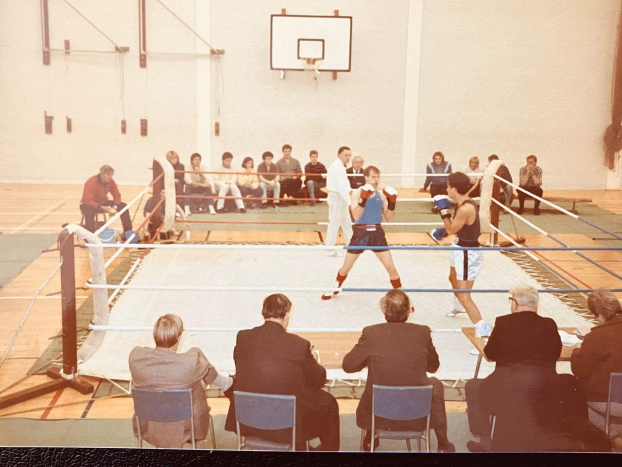 Old photo of a boxing ring, crowd watching in a sports gym and two men fighting.