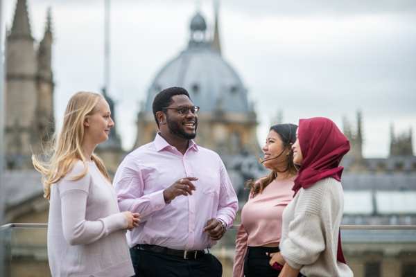 A group of four scholars standing before the Oxford skyline during daytime.