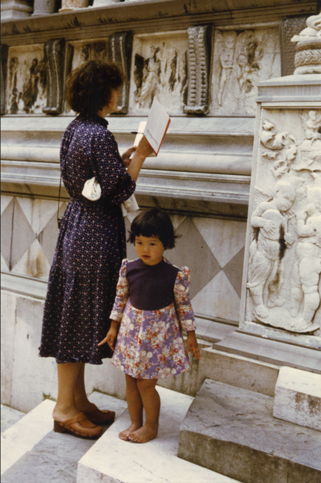 A picture showing Jaynie standing next to her little daughter, studying carved pillars and walls with a book in her hand