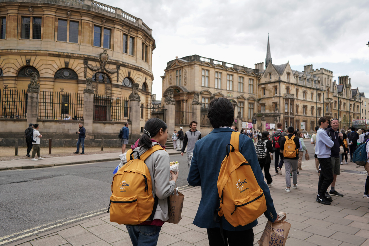 An image of two students walking through the streets of Oxford. The photo is from behind, and the two students are wearing backpacks with the Rise logo.