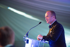John stood standing in front of a mic, wearing formal dining attire.
