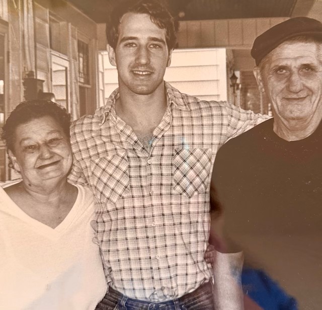 Black and white photo of Randy as a young man stood between both of his parents with his arms around them.
