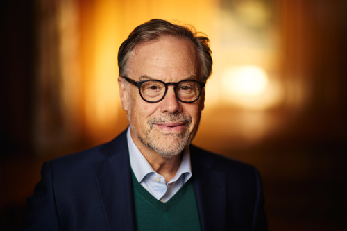 A portrait of Geoff. He is wearing a blue jacket over a dark green sweater and blue shirt.