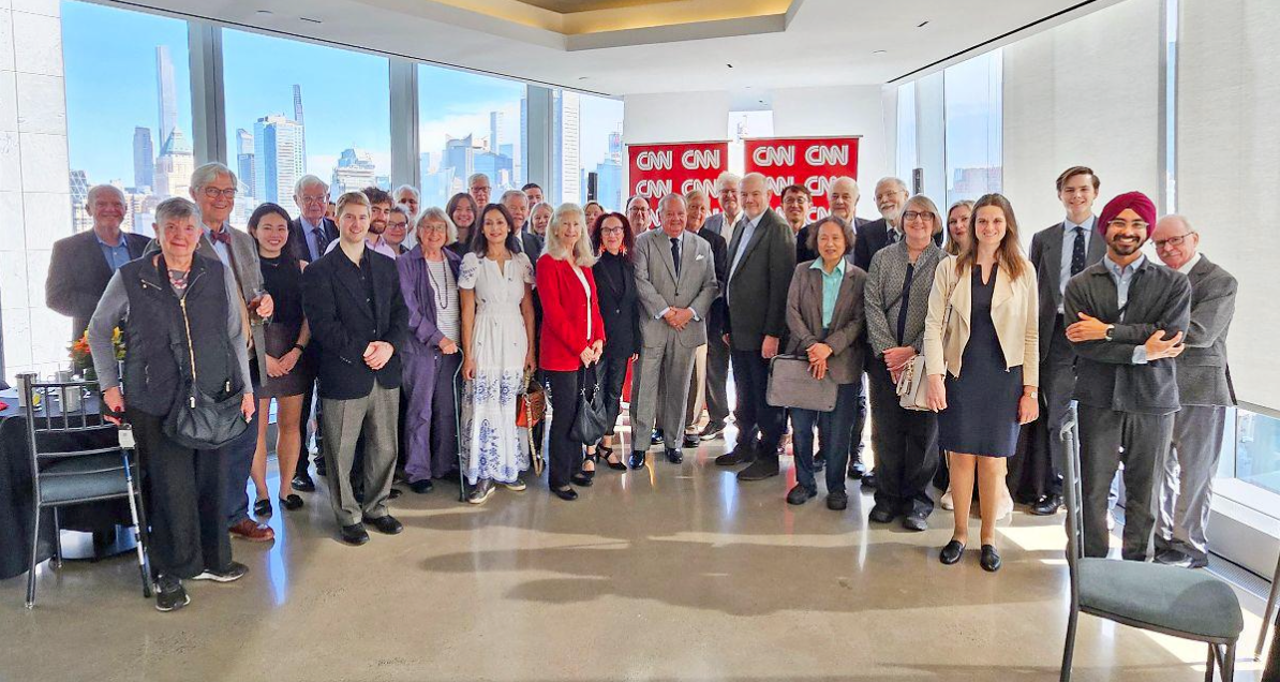 Photo of Nick with team stood all smiling into the camera in an office with a view of a city skyline on a blue day.