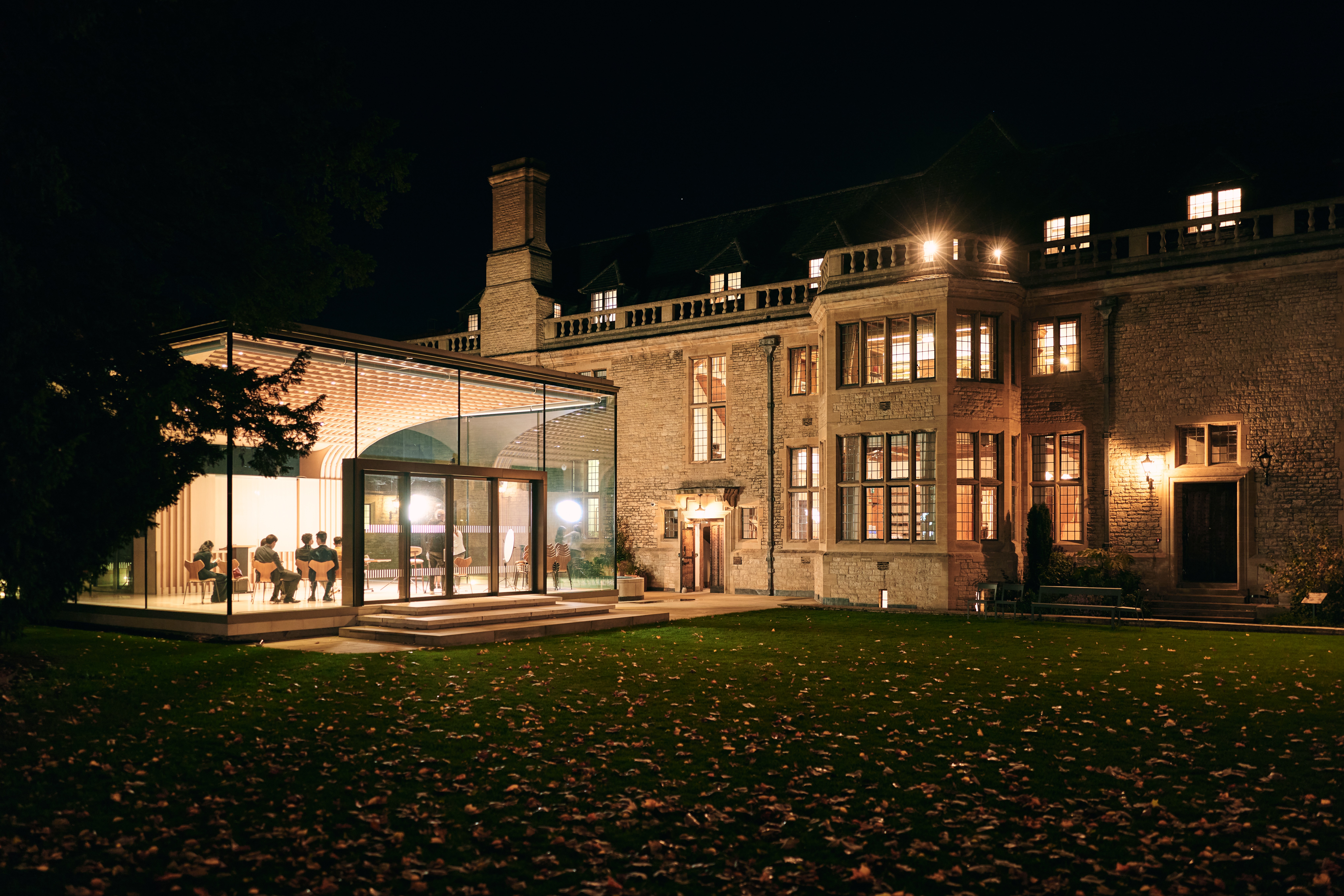 View of the glass pavilion illuminated at night with some delegates sat inside.