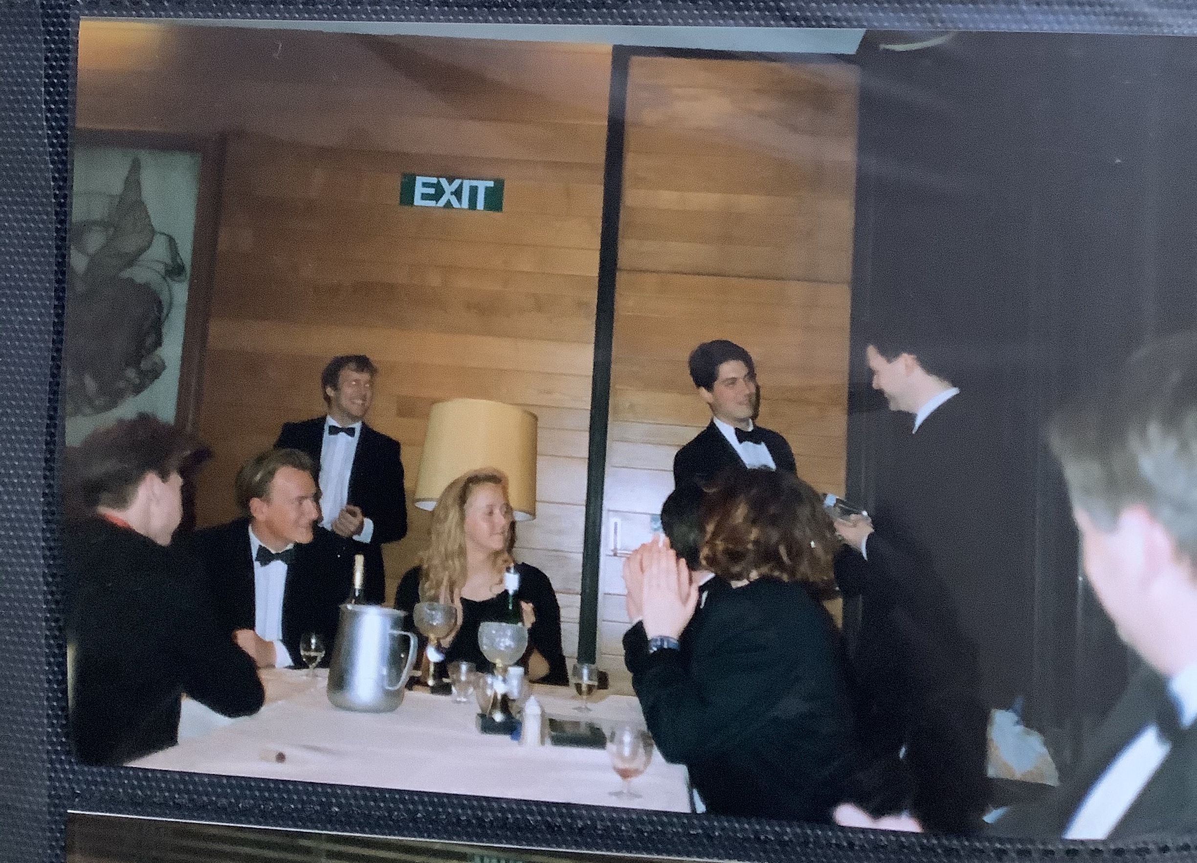 A group of students wearing suits and black tie sat around a table and talking.