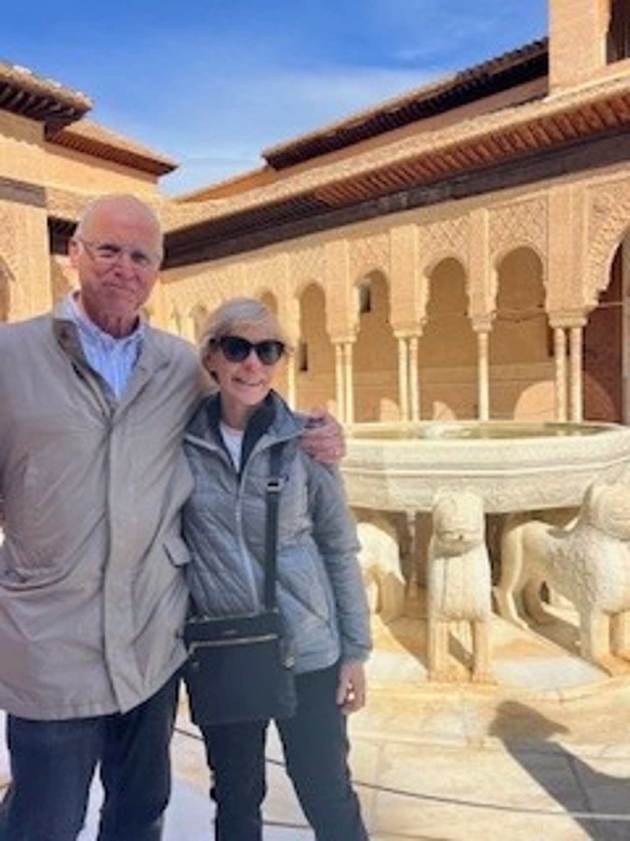 Mary with a man holding her shoulders. In the background is a sandstone building with delicate pillars and a fountain.