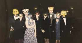 A picture showing young students in dresses and suits, with masks on their faces. Elle has a cat mask on.