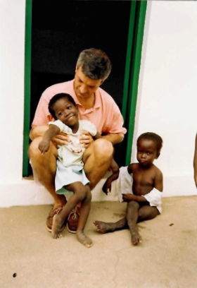 The picture shows Richard sitting on the threshold of a house, with two children around him.