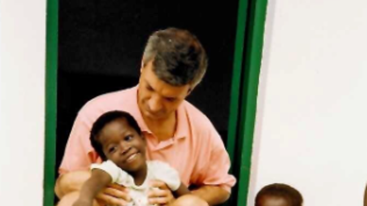 The picture shows Richard sitting on the threshold of a house, with two children around him.