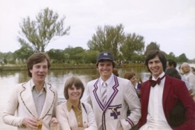 Elliot stood to the right wearing a burgundy suit, three friends to the right, all smiling and stood before an Oxford river.