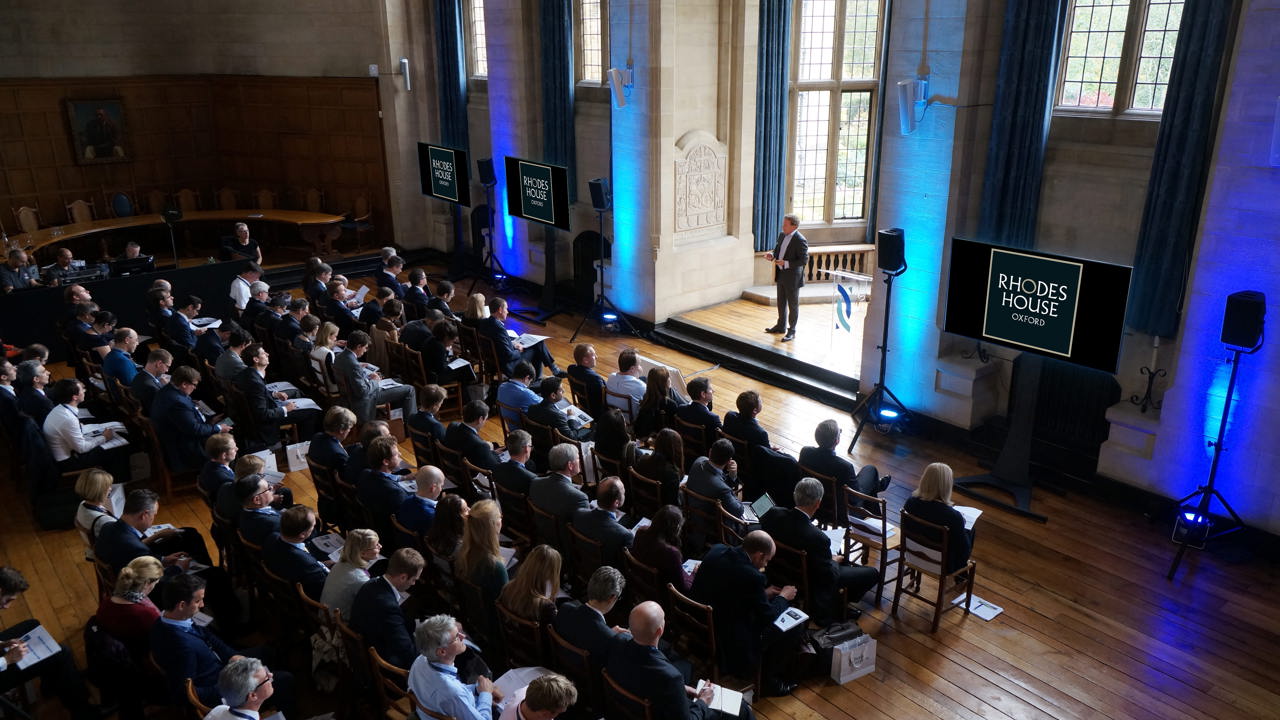 McCall MacBain Hall conference with delegates facing the speaker in the bay window, with screens on either side.