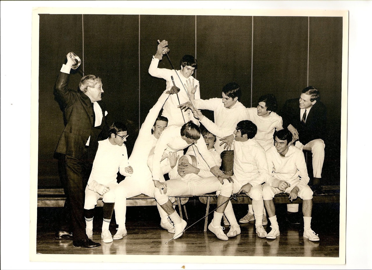 Black and white photo of group of young men fencing, wearing white.