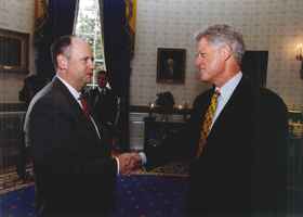 Picture showing Gary shaking hands with President Bill Clinton at the White House. Both are wearing suits.