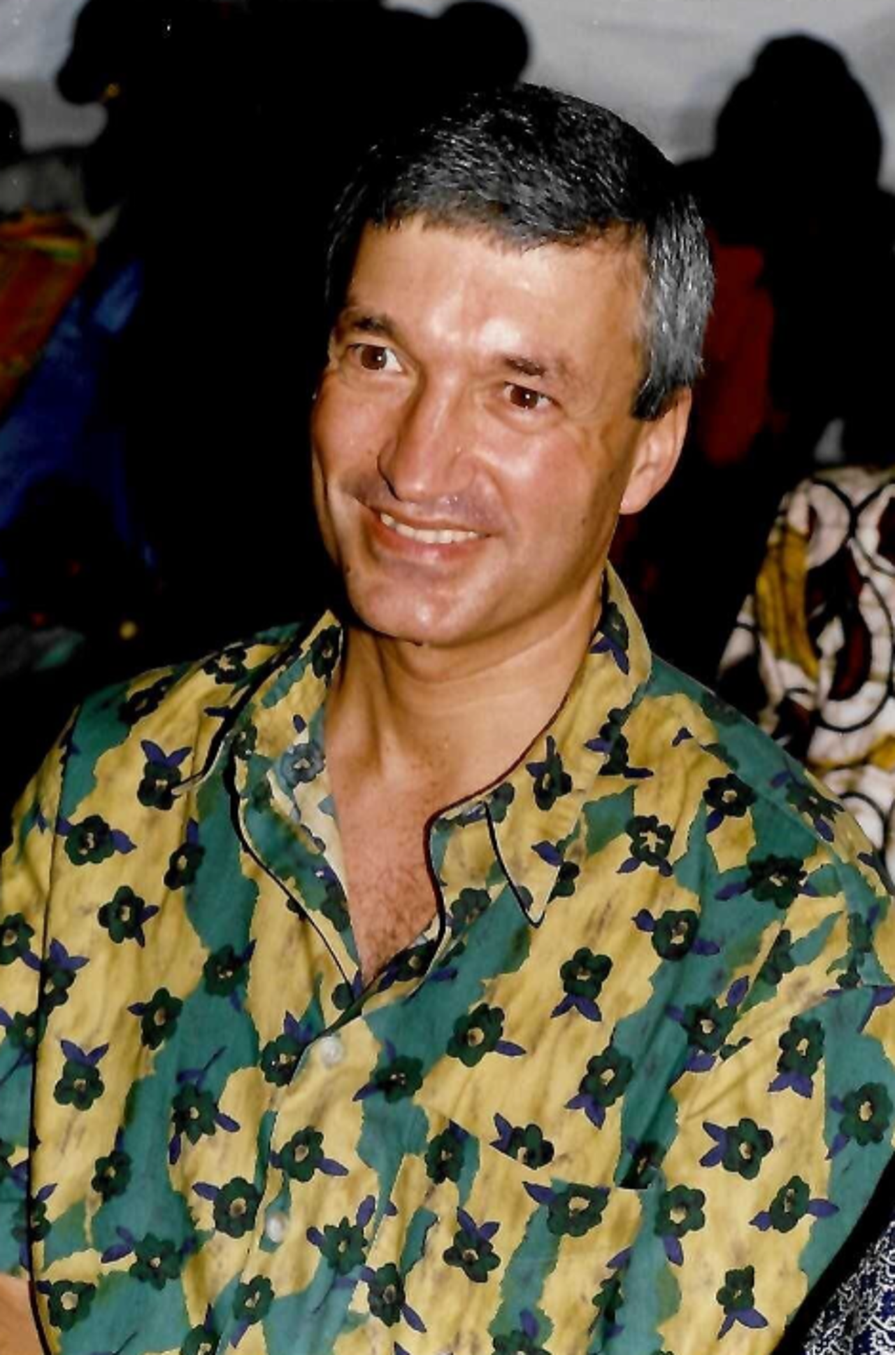 The picture shows Richard in a colorful green-and-yellow shirt with dark patterns. He is smiling at the camera.