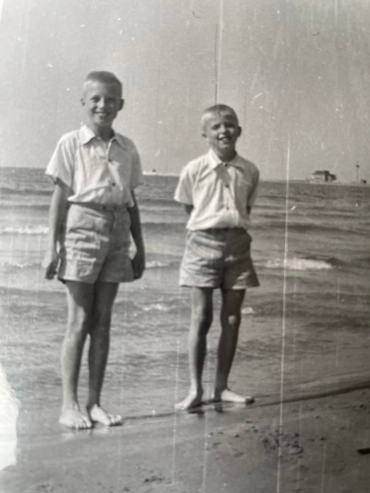 Black and white photo of Geza and his brother stood at the shore of a beach.