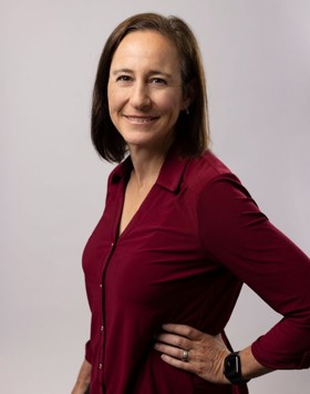 Jane stood, wearing a burgundy shirt, with her left arm against her hip and smiling into the camera.
