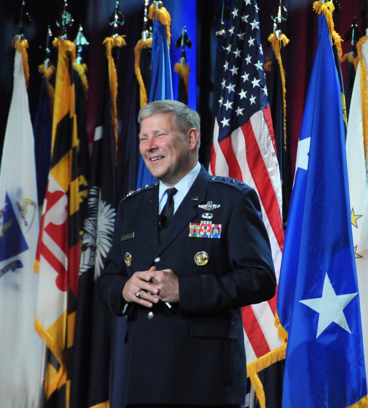 Portrait photo of Chris stood before flags, and wearing uniform with medals.