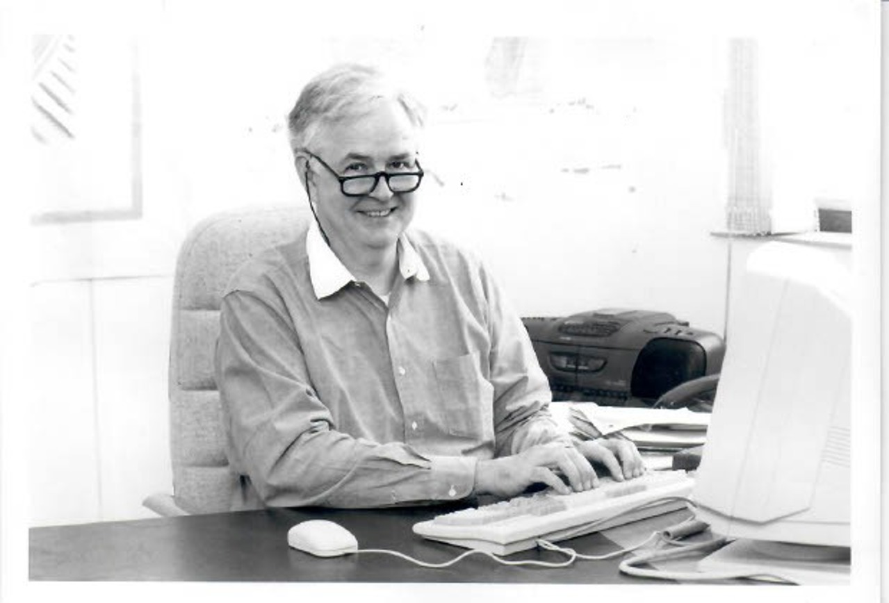 A black-and-white picture of Norton at a table, sitting in front of his computer, his fingers on the keyboard.