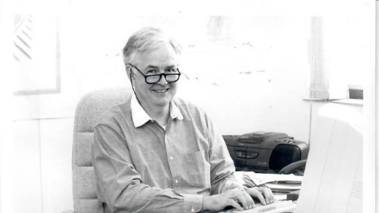 A black-and-white picture of Norton at a table, sitting in front of his computer, his fingers on the keyboard.