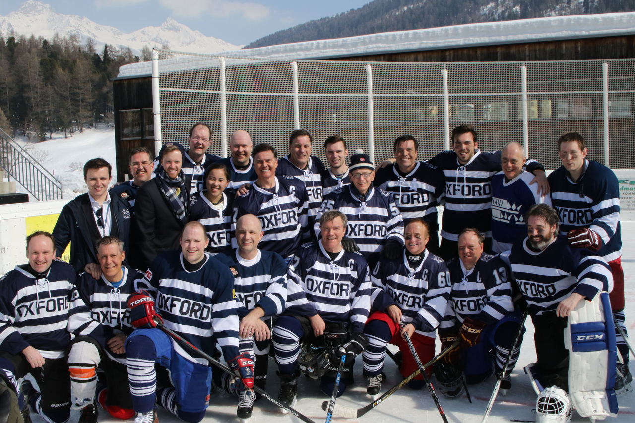 Large group all wearing hockey outfits stood on a snowy mountain and posing.