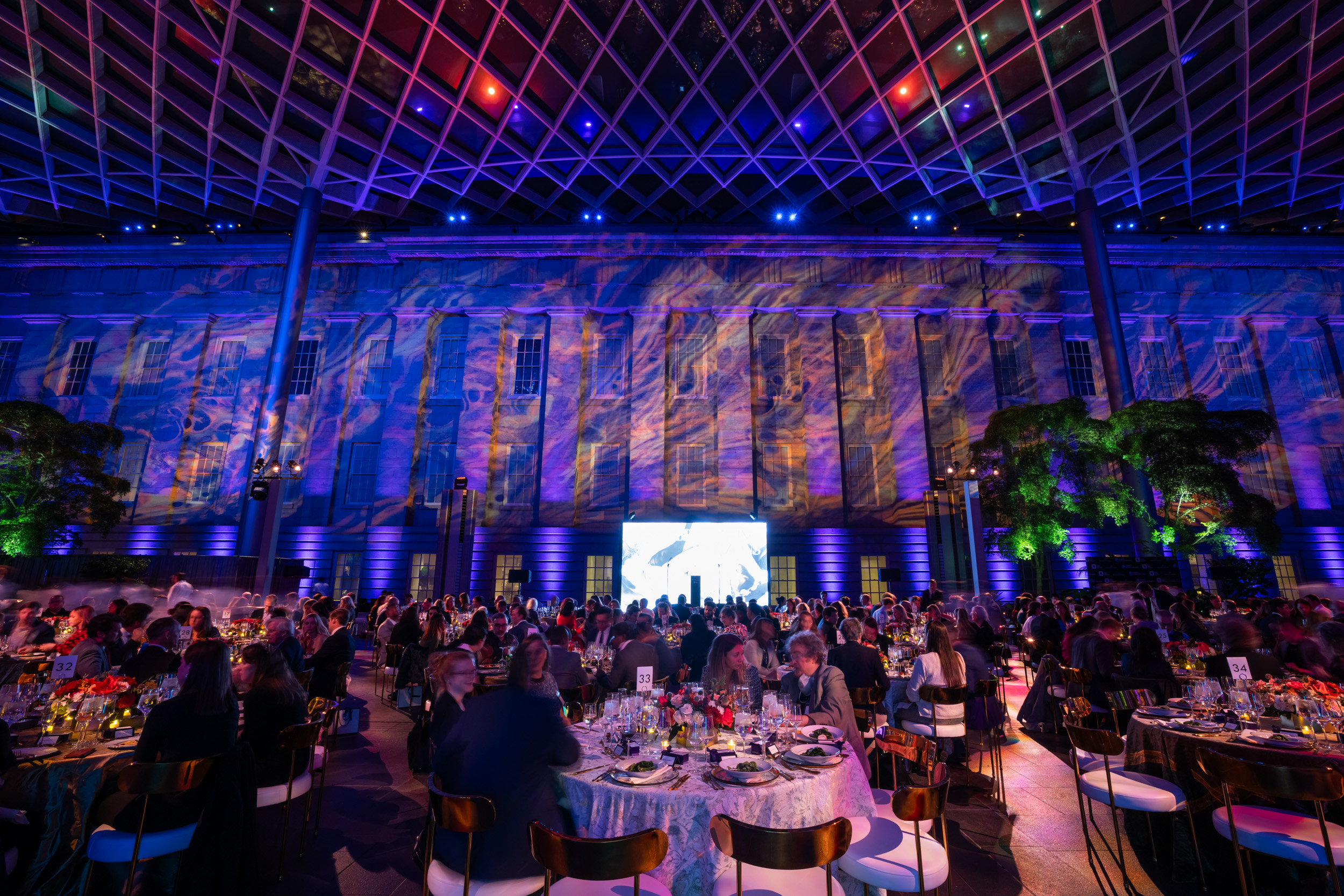 A gala dinner being hosted inside a museum space with high ceilings and colourful projections on the walls.
