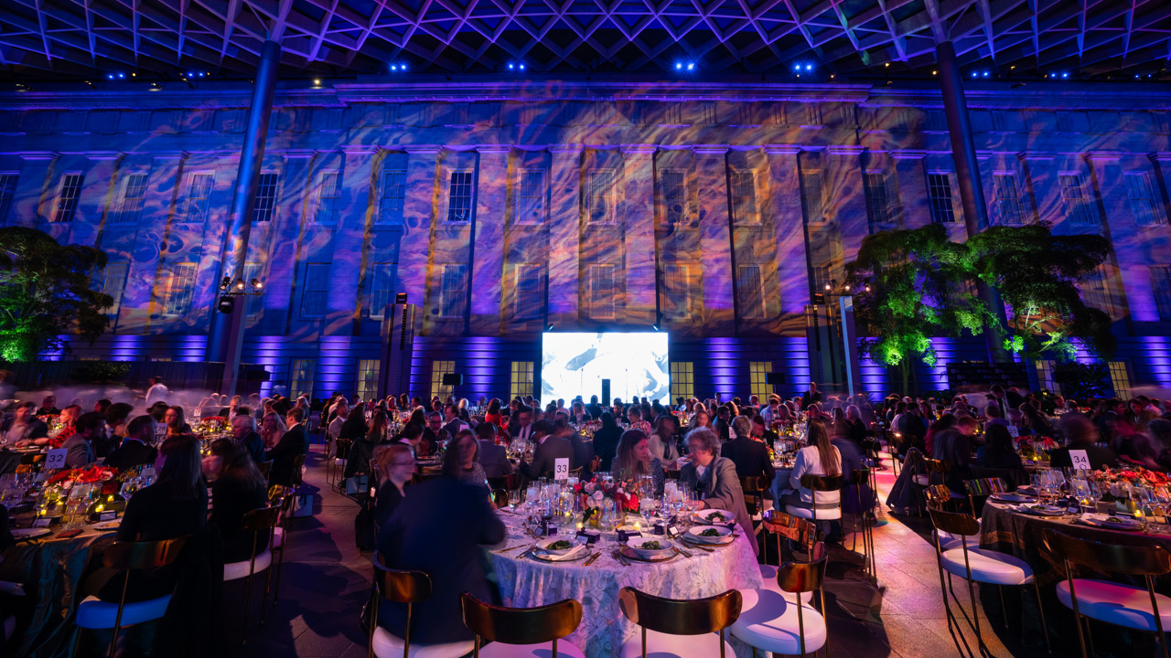 A gala dinner being hosted inside a museum space with high ceilings and colourful projections on the walls.