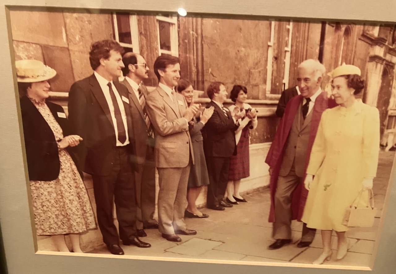 The picture shows Queen Elizabeth II walking on a pavement while a row of people claps, among them Bob