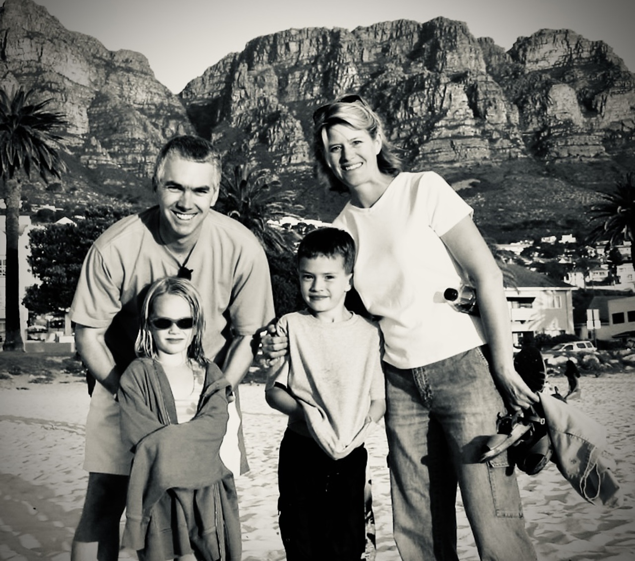 A black-and-white picture of Charles with Kris and their two children on a beach in Cape Town, with rocky hills in the background