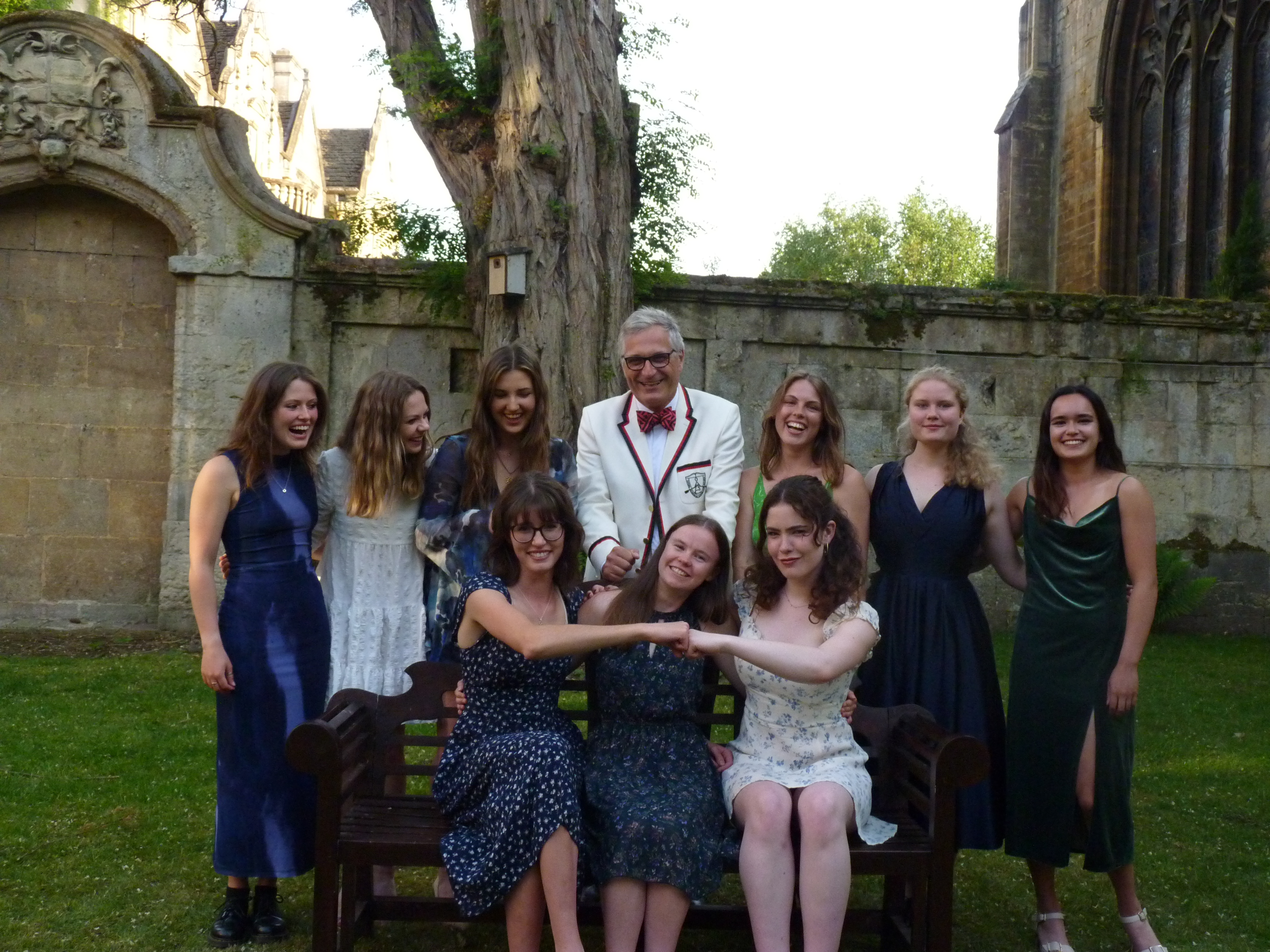 Agyris is stood in the middle of a group of female university students. He is wearing a white blazer and red bow tie.