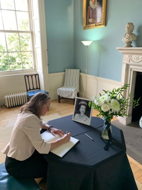 Jenny sat on the floor writing a card with a black and white photo of Queen Elizabeth II in front of her.