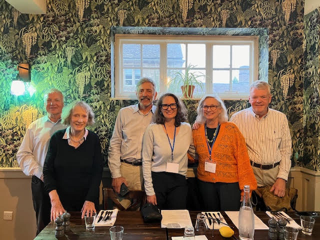 A group of alumni stood smiling with a dinner table before them.