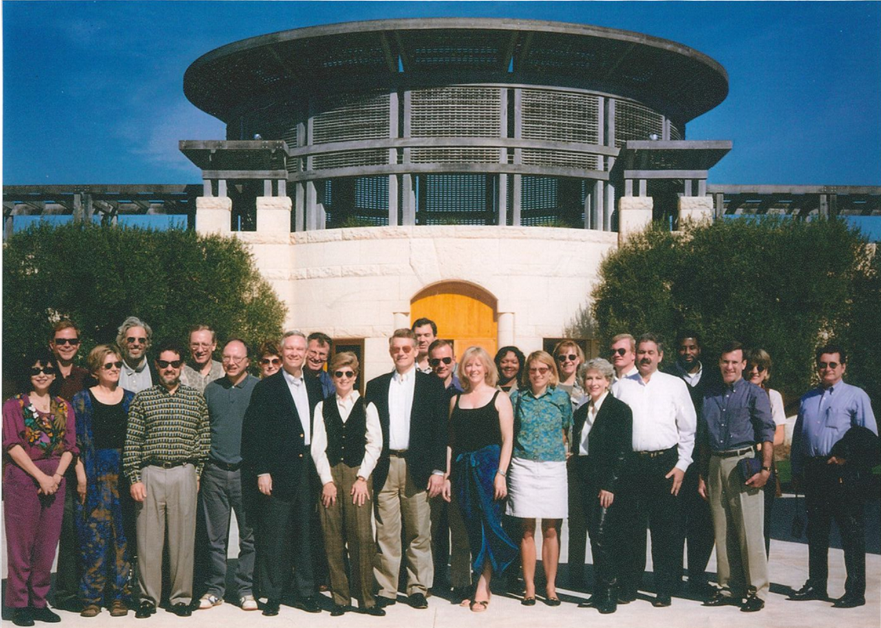 The picture shows a large group of people standing in front of a glass building.